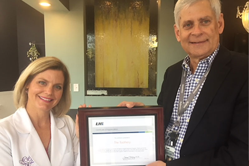 doctor posing for picture with plaque in hand within the dental center