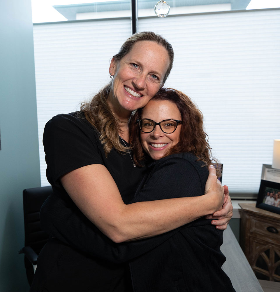 staff member and Invisalign patient smiling while hugging in a warm embrace